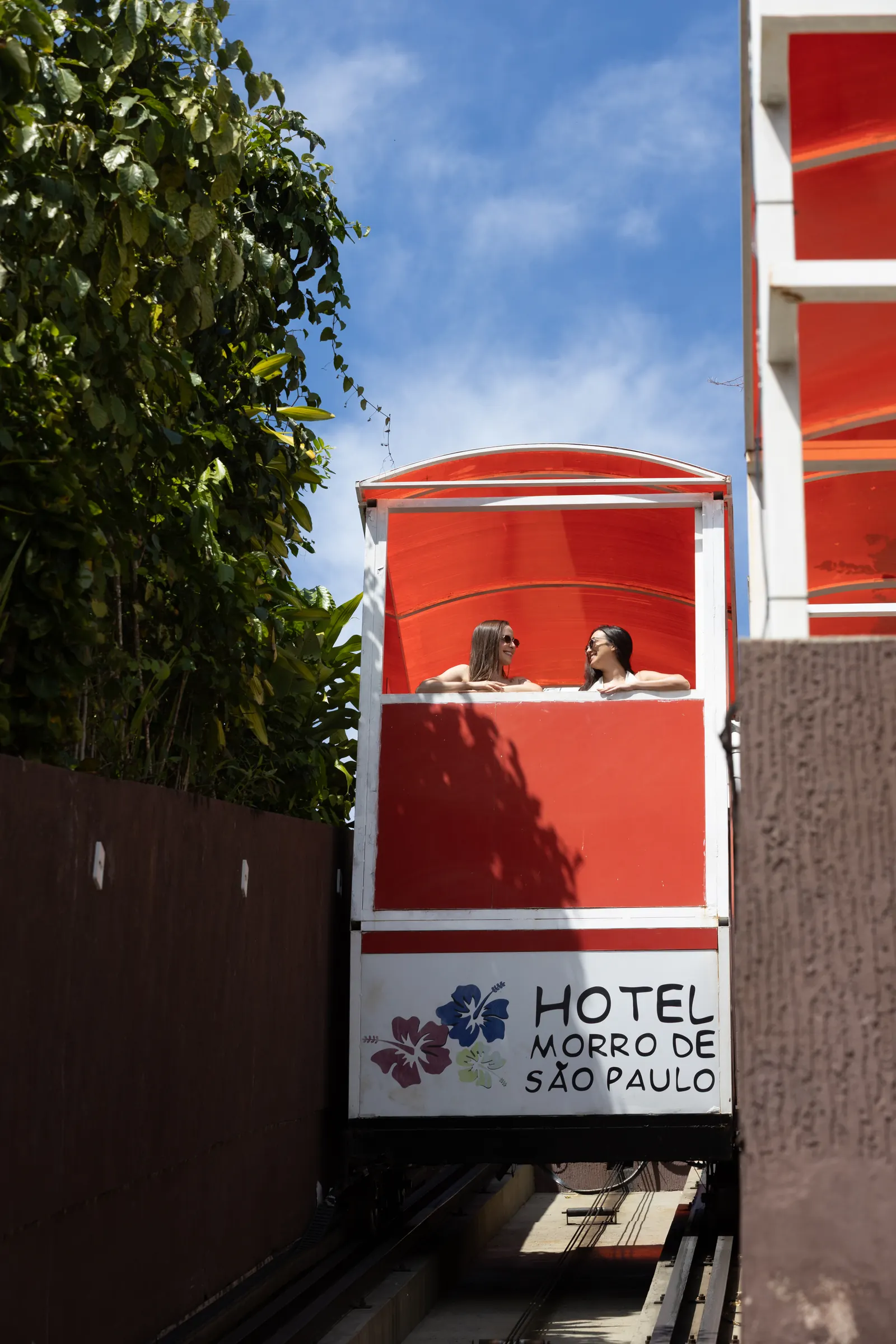 Bondinho vermelho com o nome do Hotel Morro de São Paulo entre o muro de madeira e a vegetação