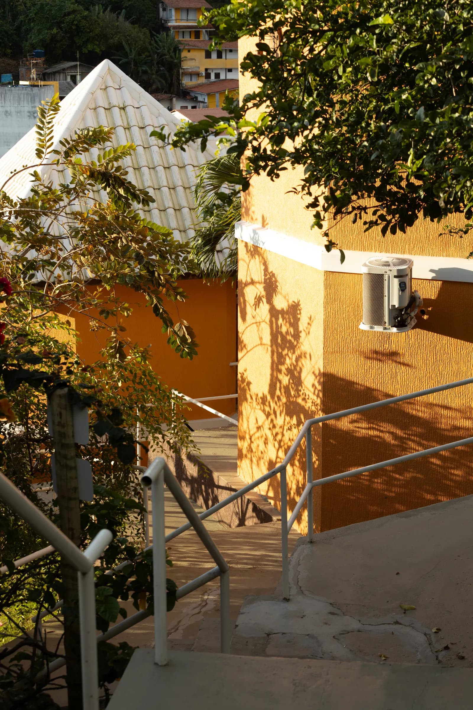 Fachadas cor de ocre do hotel entre árvores, escadas e telhados brancos