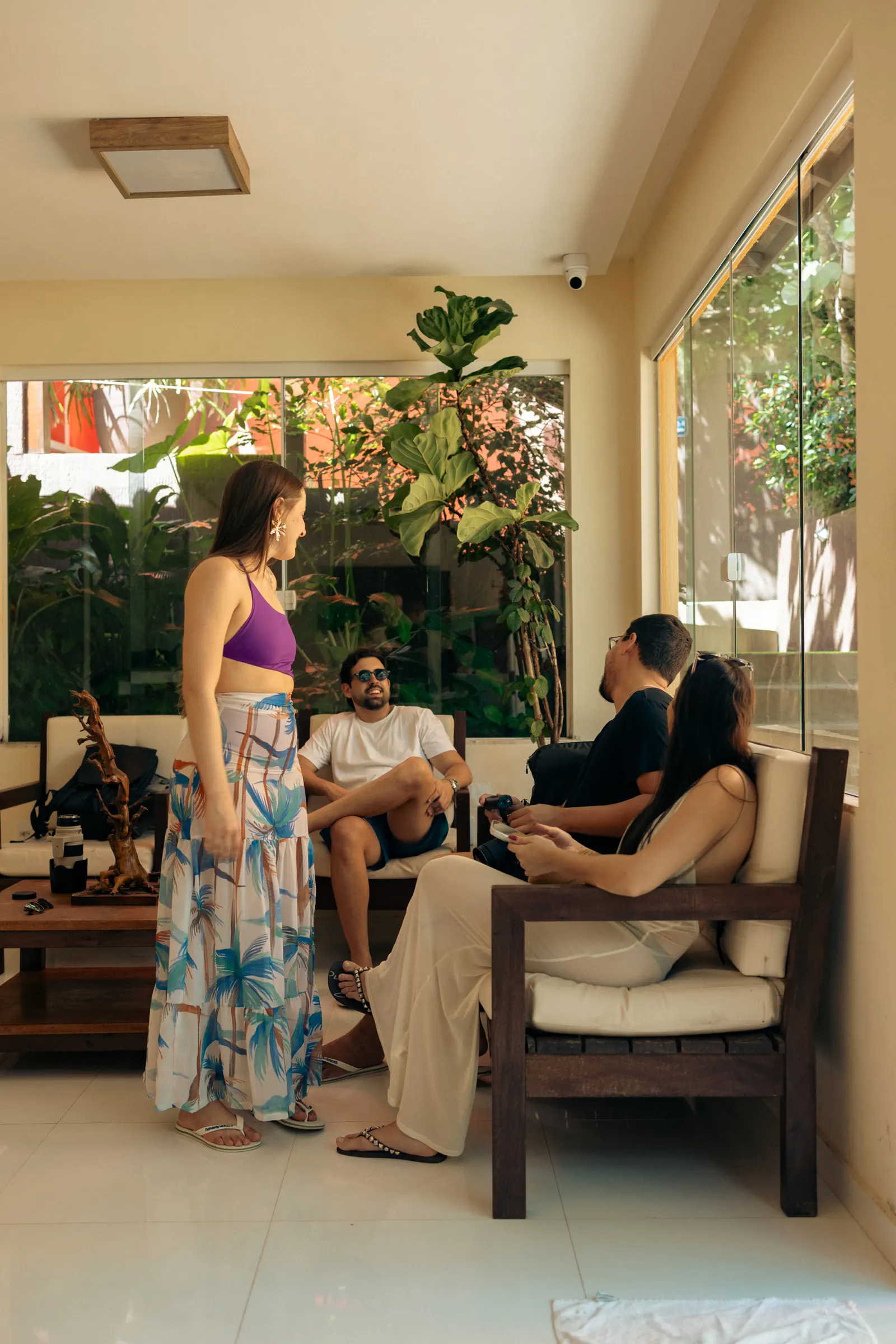 Sala de estar do hotel com sofás de madeira, janelas de vidro e jardim ao fundo